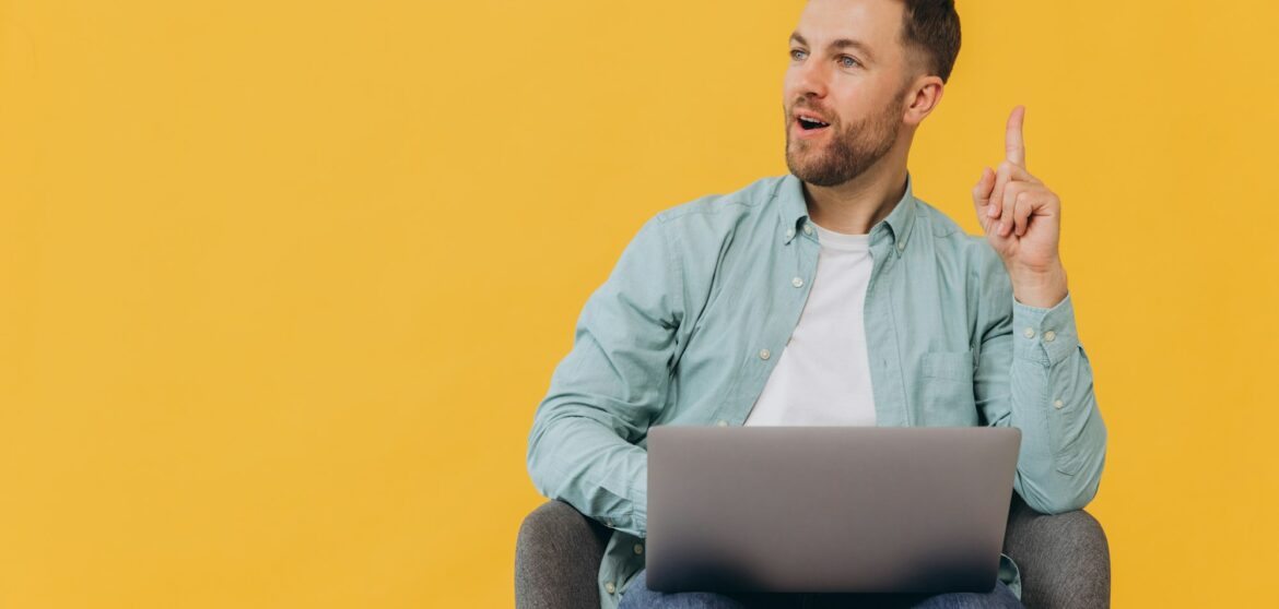 Unshaven man in trendy mint shirt sit in chair hold use work on laptop pc computer and show finger