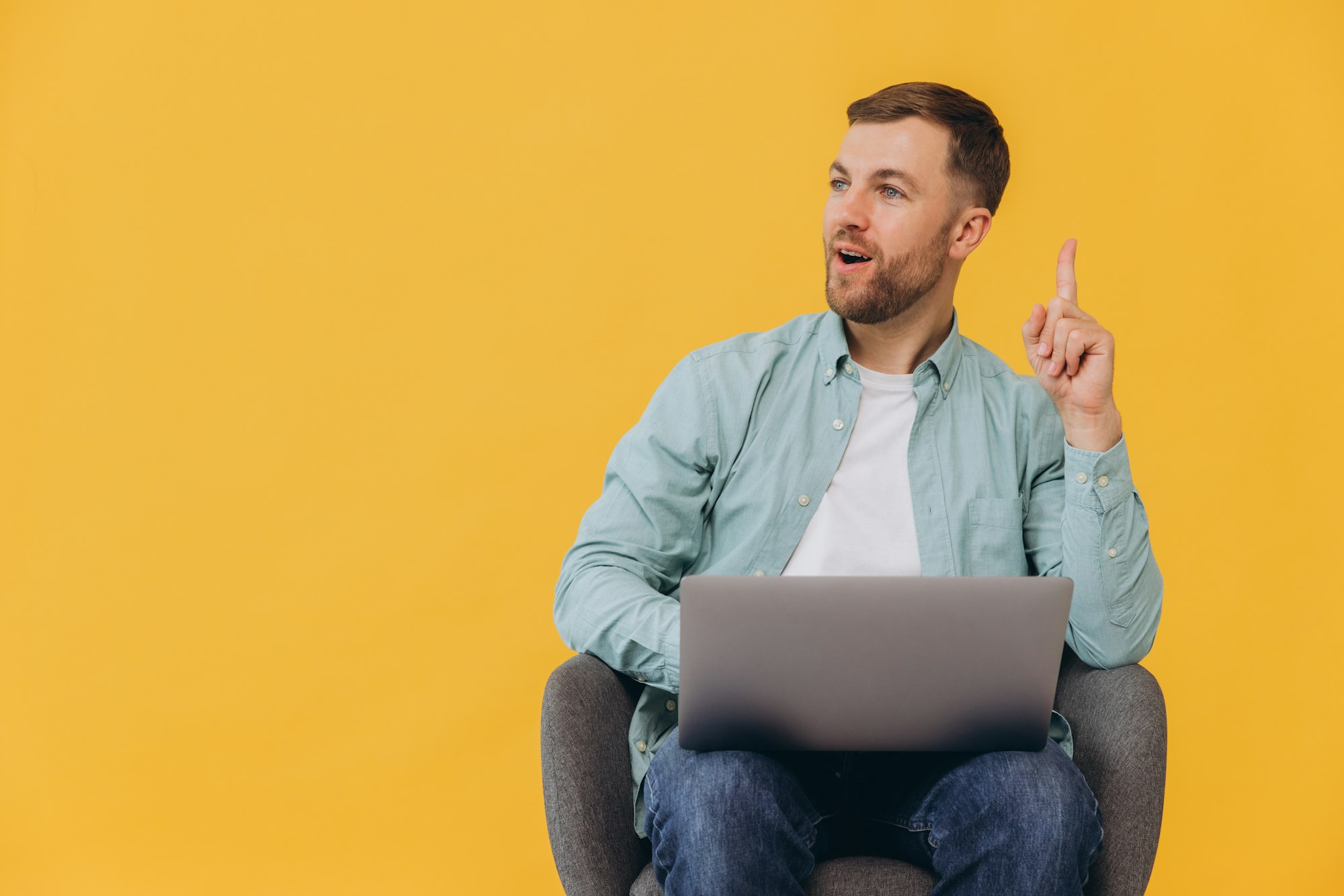 Unshaven man in trendy mint shirt sit in chair hold use work on laptop pc computer and show finger