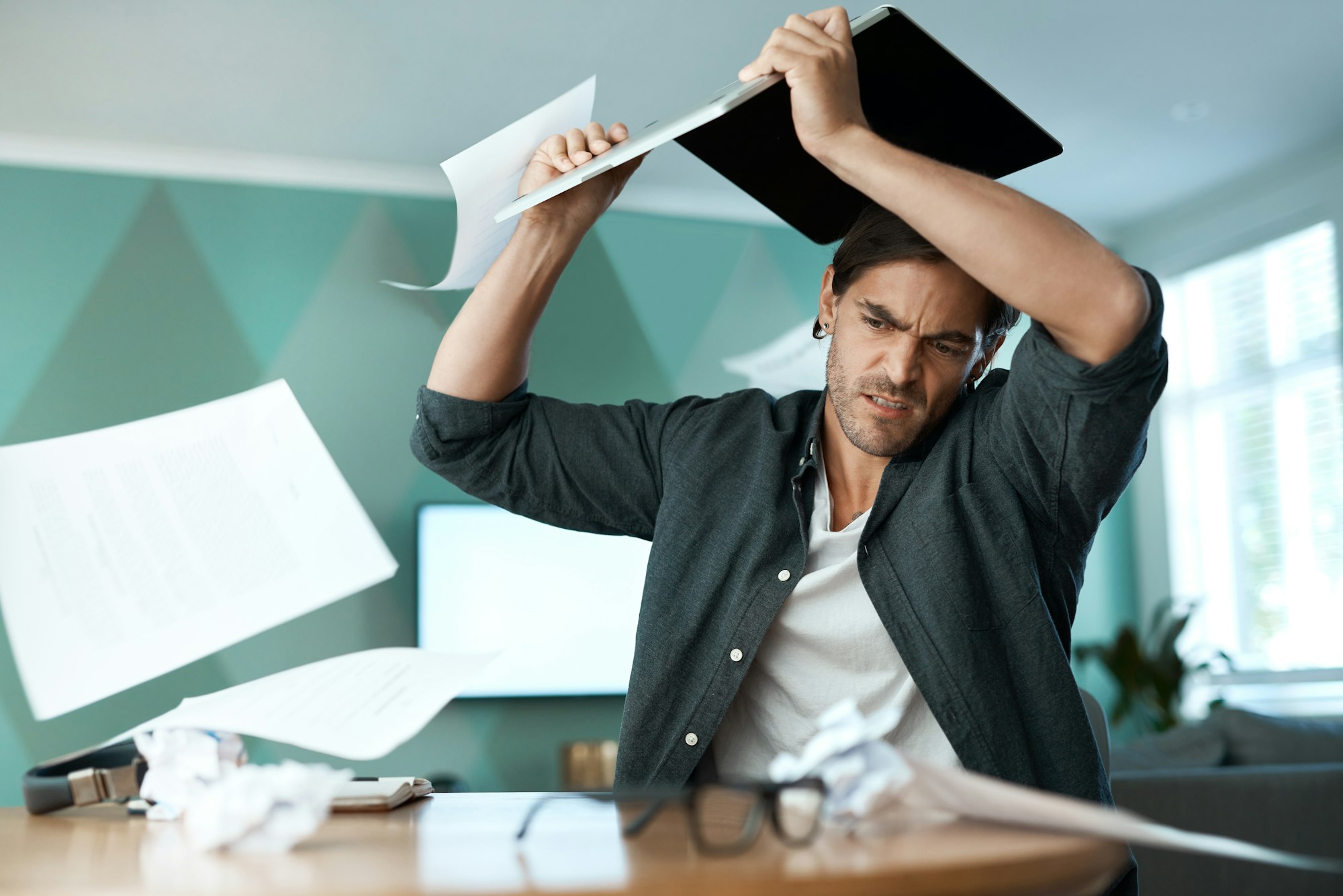 Why is this thing not working. Shot of a young man smashing a laptop on a table at home.